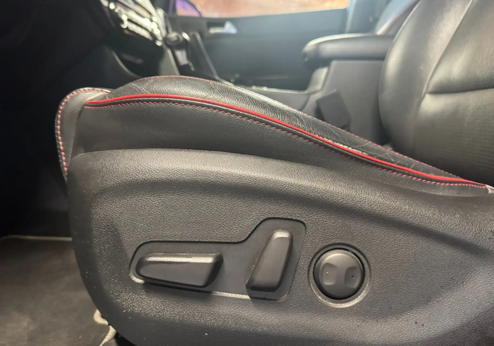 Gros plan sur les commandes électriques du siège avant en cuir noir avec surpiqûres rouges du Kia Sportage 2019.