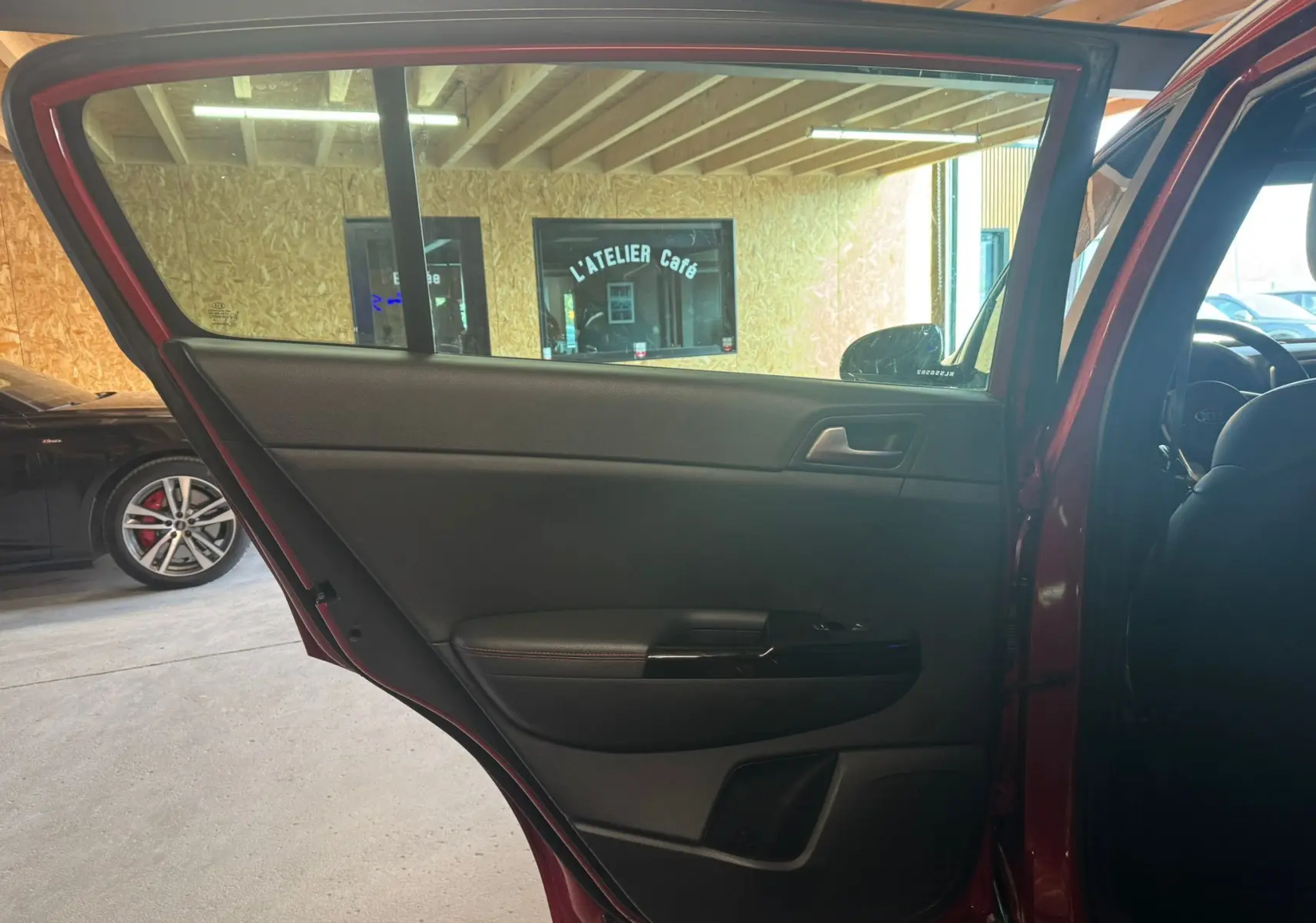 Vue intérieure de la porte arrière gauche rouge d’un Kia Sportage 2019, avec garniture noire et poignée intégrée.