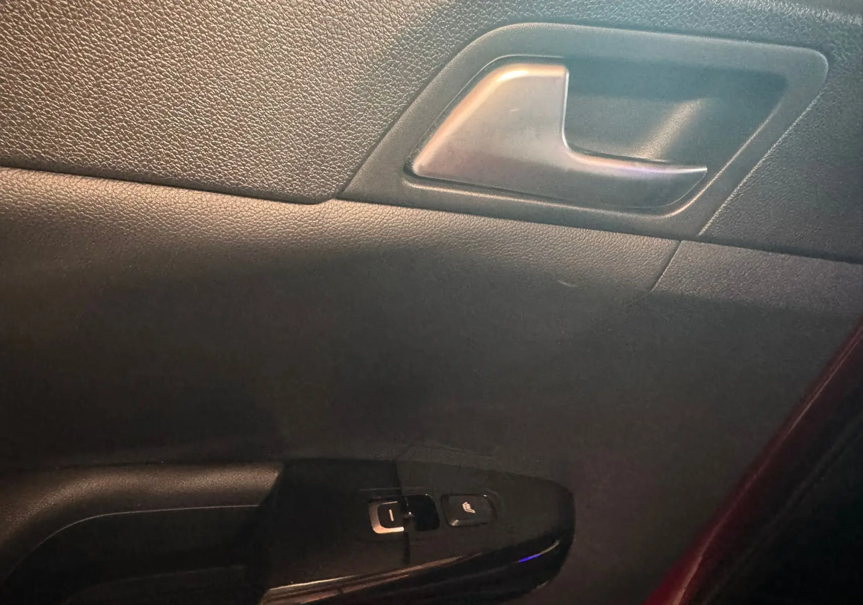 Gros plan sur la poignée intérieure et les commandes de fenêtre côté conducteur du KIA Sportage rouge, finition GT Line.