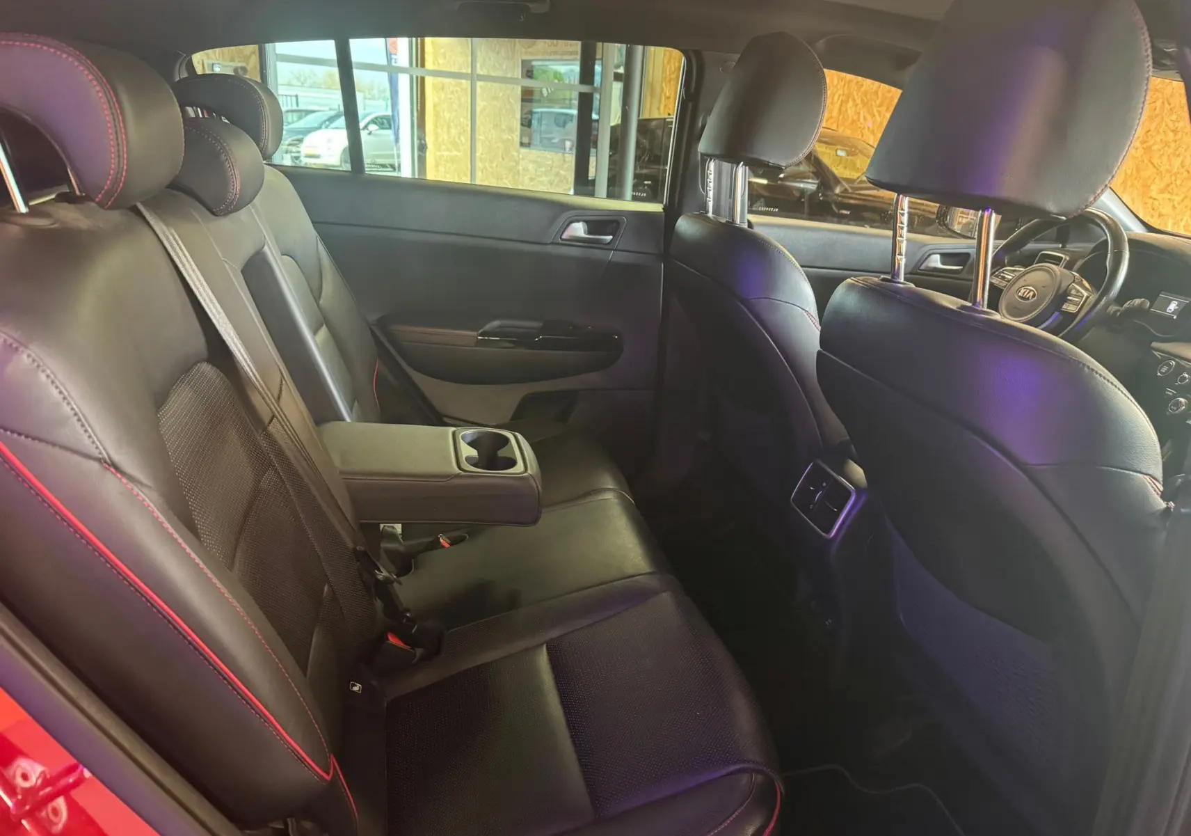 Intérieur noir cuir du Kia Sportage rouge, vue côté gauche arrière montrant les sièges et accoudoir central avec porte-gobelets.