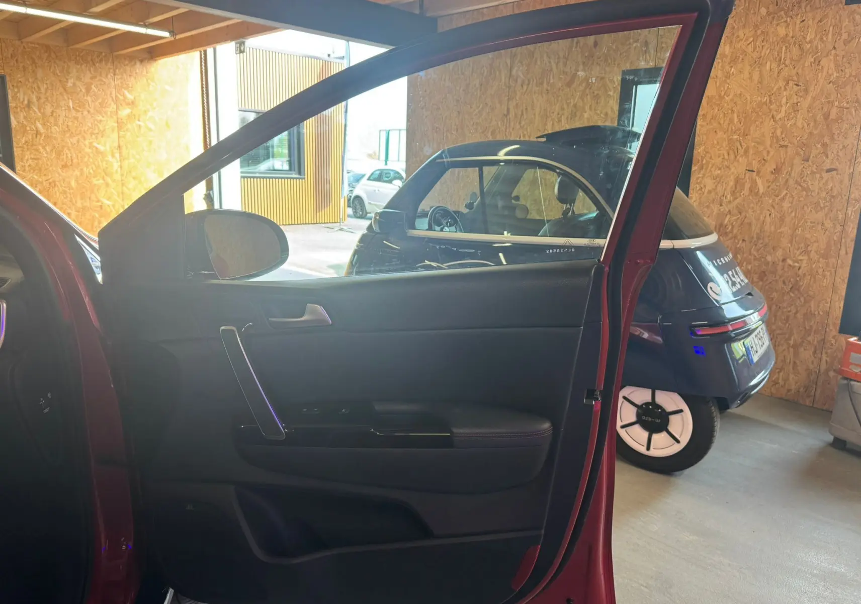 Vue intérieure de la porte avant gauche rouge du Kia Sportage 2019, mettant en valeur la garniture noire et la poignée argentée.