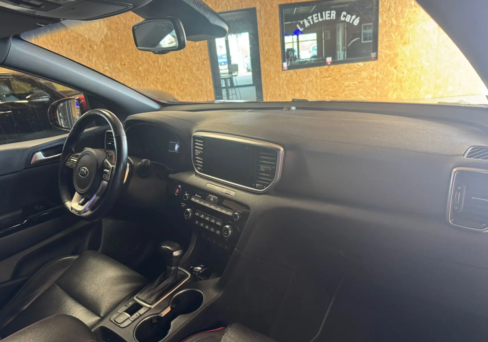 Vue intérieure côté conducteur du Kia Sportage 2019, tableau de bord noir avec écran tactile et volant cuir.
