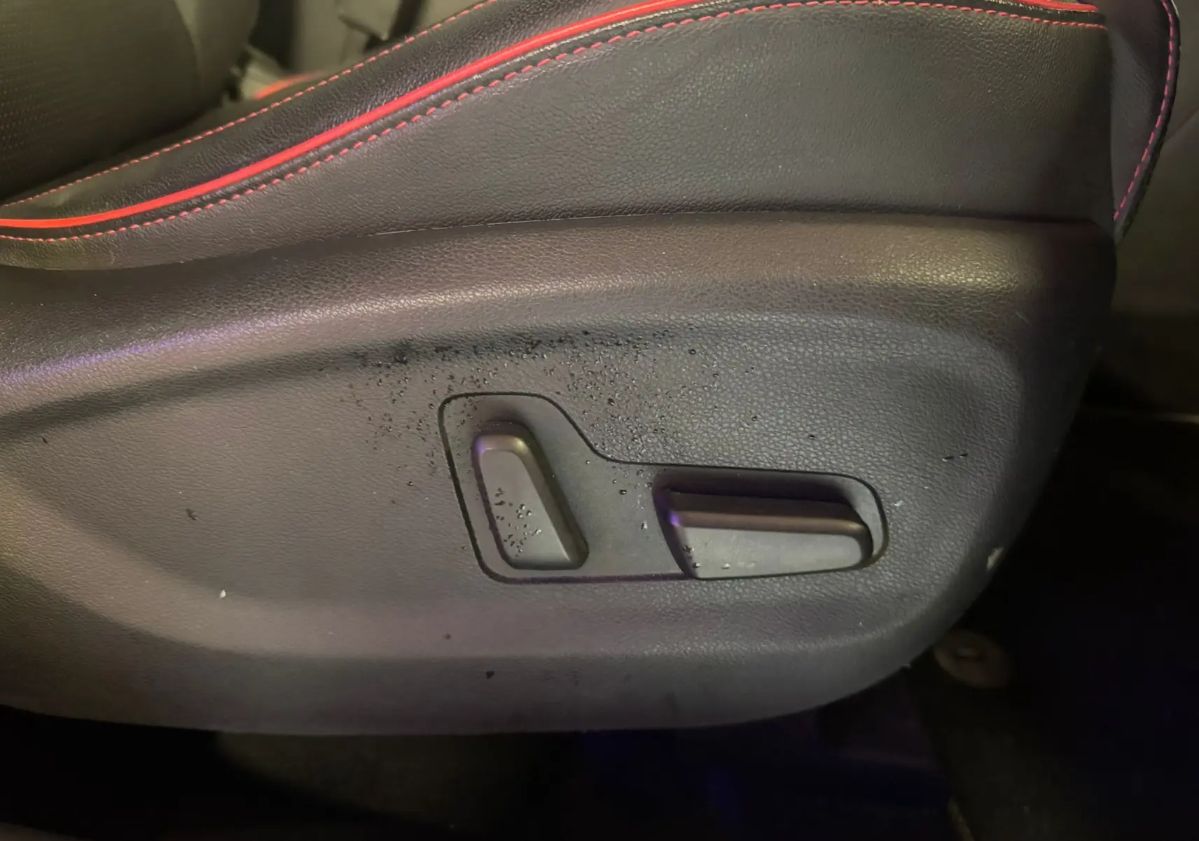 Détail des commandes de réglage électrique du siège avant en cuir noir avec surpiqûres rouges d’un KIA Sportage rouge 2019.