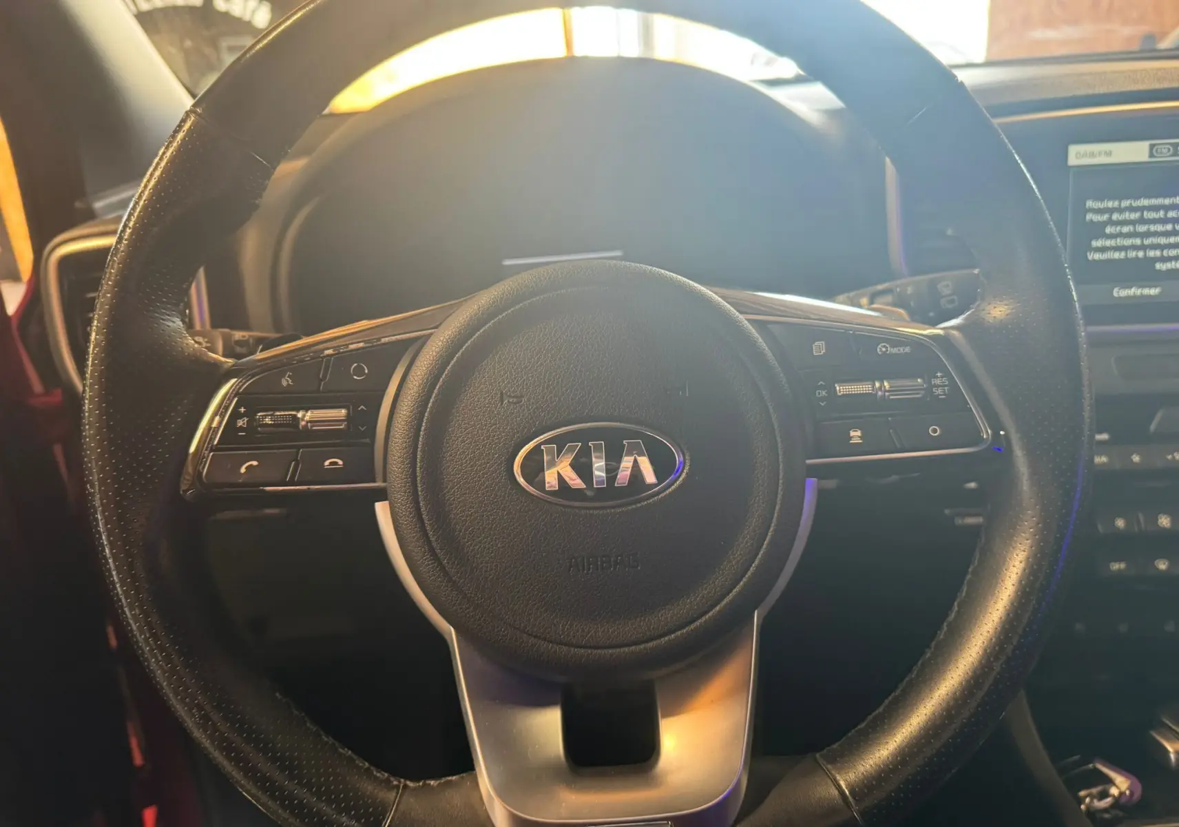 Gros plan sur le volant cuir noir du Kia Sportage rouge 2019, avec commandes intégrées et logo central visible.