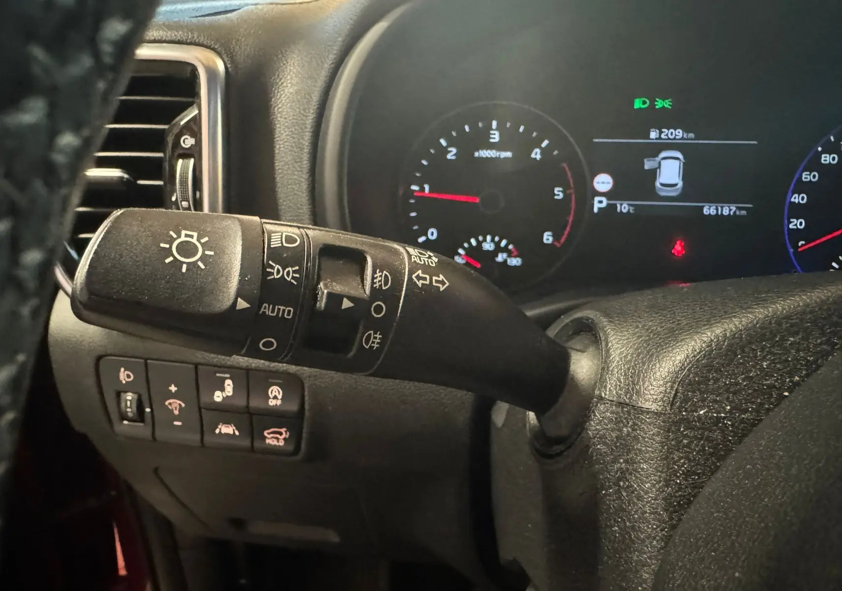 Gros plan sur la commande des phares et le tableau de bord numérique d'un KIA Sportage rouge, version 2019.