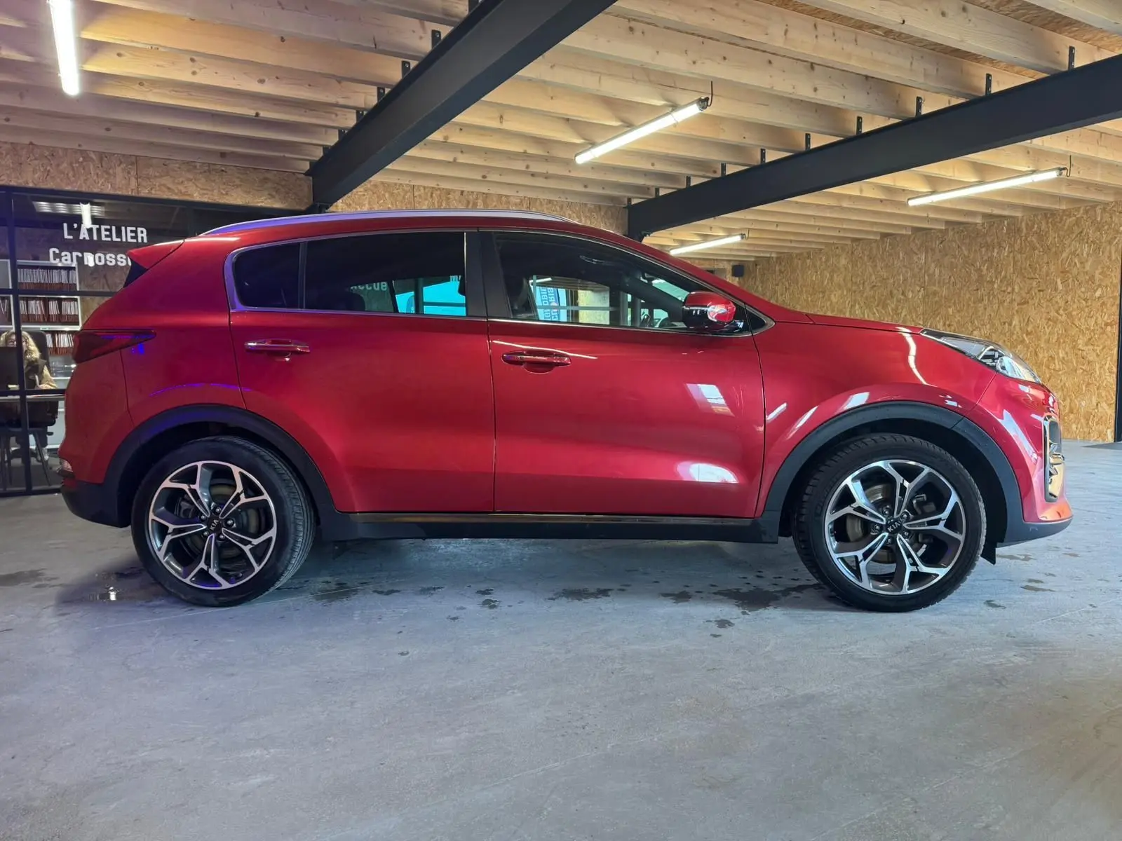 Vue de profil droit d'un KIA Sportage rouge 2019, version 1.6 CRDI GT Line, avec jantes alliage et toit noir.