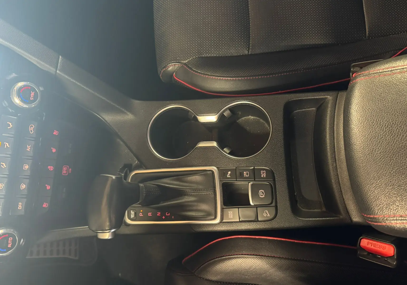 Vue plongeante sur la console centrale noire du Kia Sportage 2019, avec levier de vitesse automatique et coutures rouges.