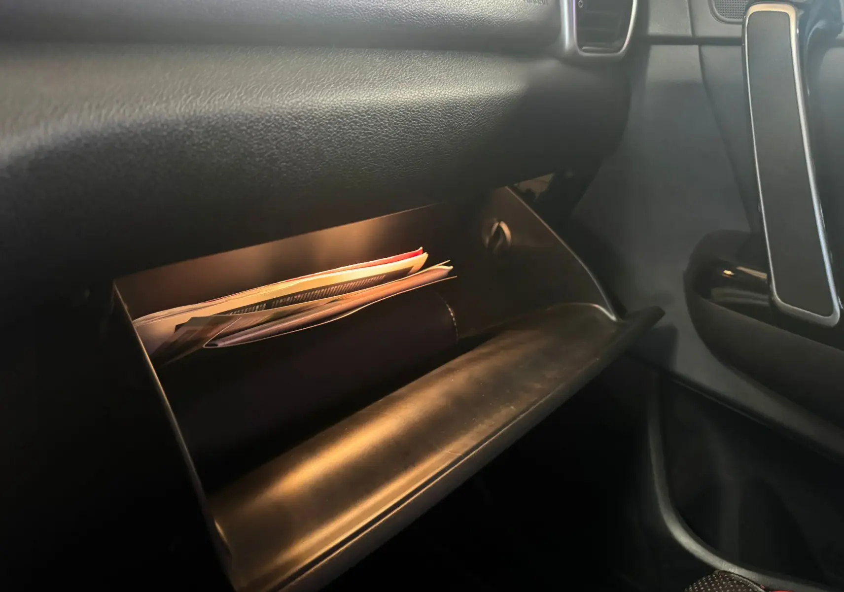 Gros plan sur la boîte à gants ouverte côté passager du Kia Sportage 2019, intérieur noir avec documents visibles.