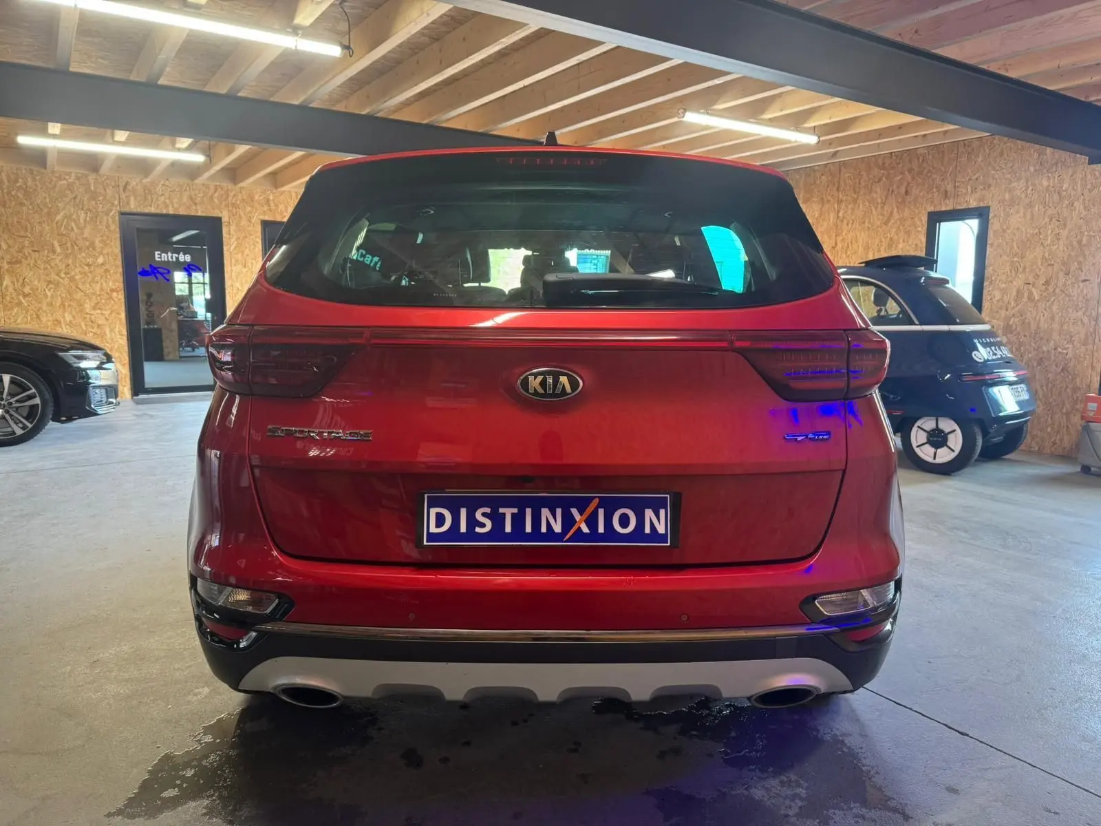 Vue arrière d'un KIA Sportage rouge 2019 en intérieur, avec feux LED et double sortie d'échappement visibles.