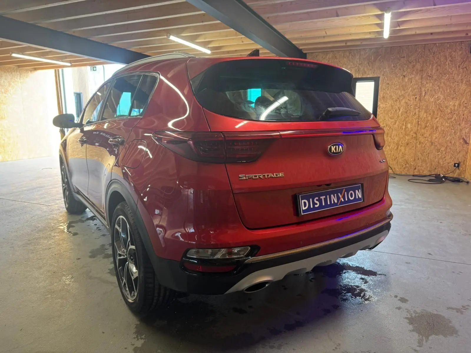 Vue 3/4 arrière droite d'un KIA Sportage rouge 2019 avec feux arrière sombres et double sortie d'échappement.