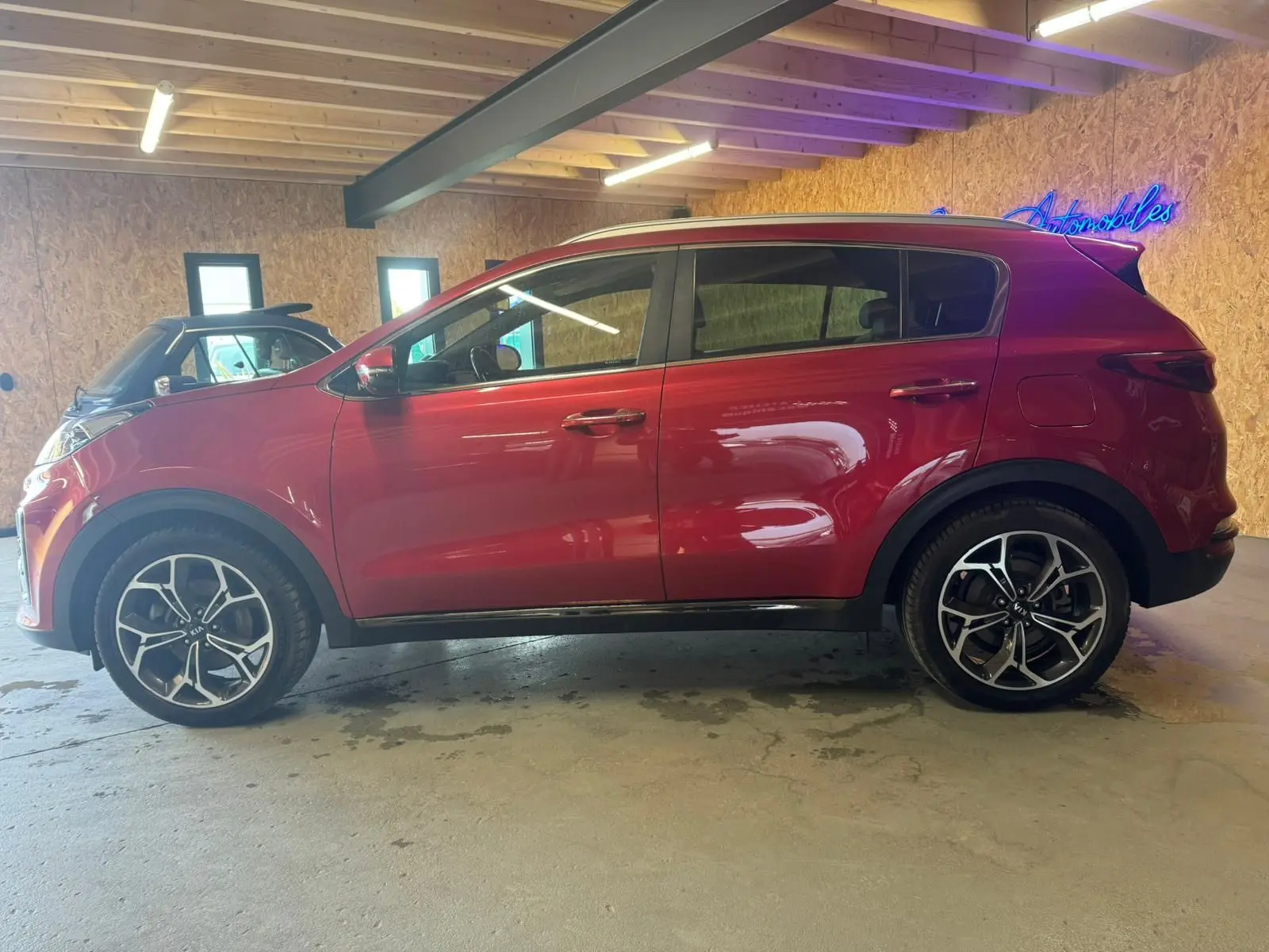 Vue de profil côté gauche d'un KIA Sportage rouge 2019, avec jantes alliage noires et détails sportifs visibles.
