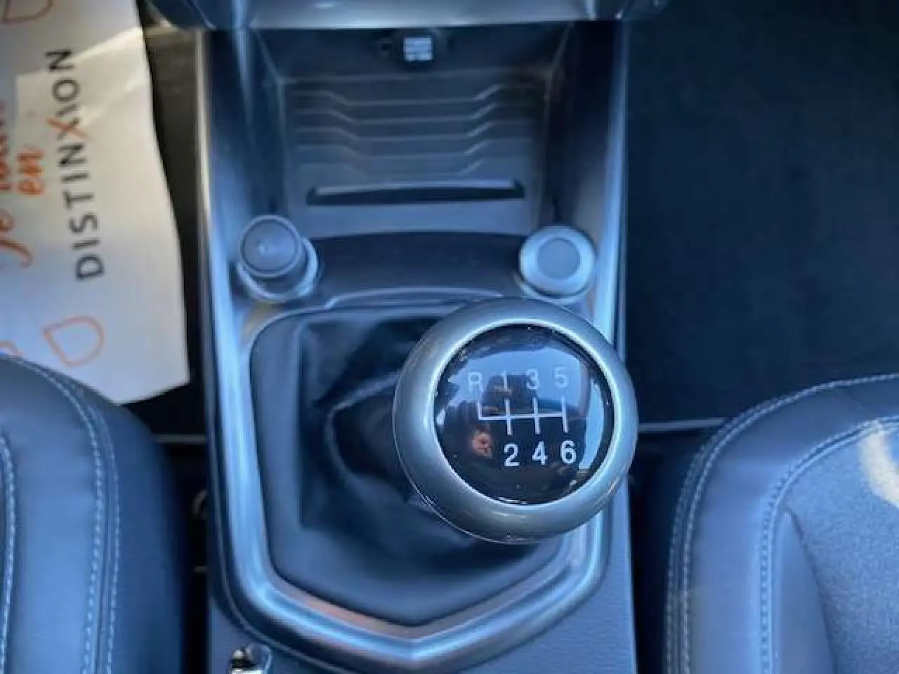 Le levier de vitesses manuel noir du SSANGYONG TIVOLI 160 e-XDi 2WD vu de dessus entre les sièges en cuir gris foncé.