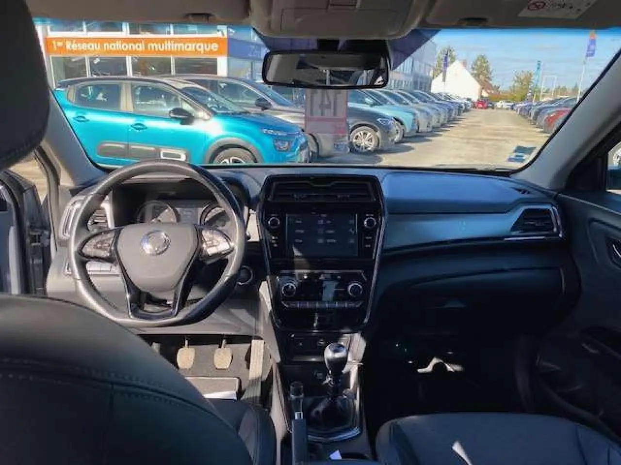 Vue intérieure avant du SsangYong Tivoli gris foncé montrant le tableau de bord et le volant cuir avec écran tactile central.