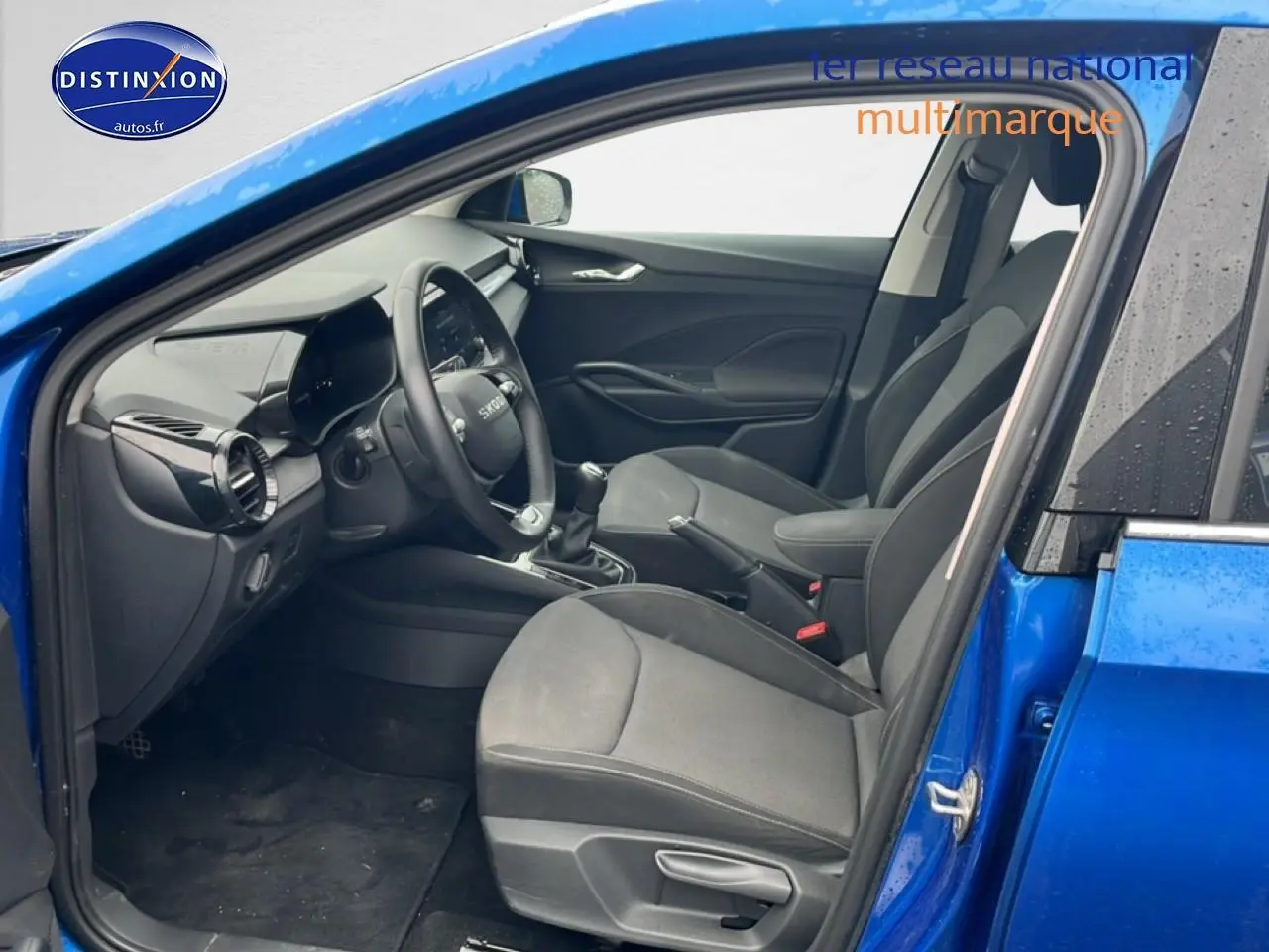Vue intérieure côté conducteur d'une Skoda Fabia bleu 2025 avec sièges noirs et volant multifonction cuir.