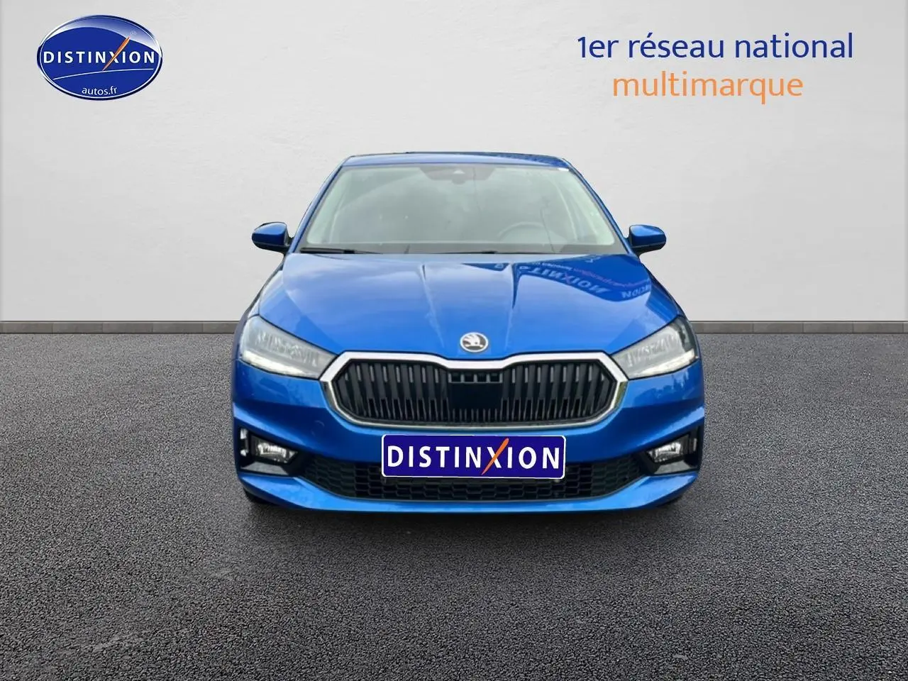 Vue frontale d'une Skoda Fabia bleue 2025 avec calandre noire et phares LED, sur fond neutre gris.