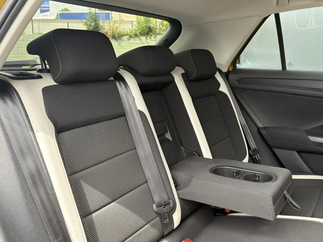 Vue intérieure sur la banquette arrière du Volkswagen T-Roc 1.5 TSI jaune curcuma, avec accoudoir central déplié.