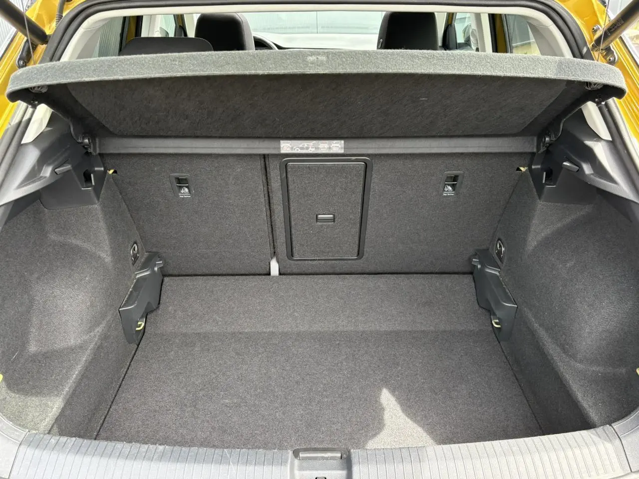 Vue intérieure du coffre ouvert du Volkswagen T-Roc jaune curcuma, montrant le plancher et la cloison arrière en tissu gris.