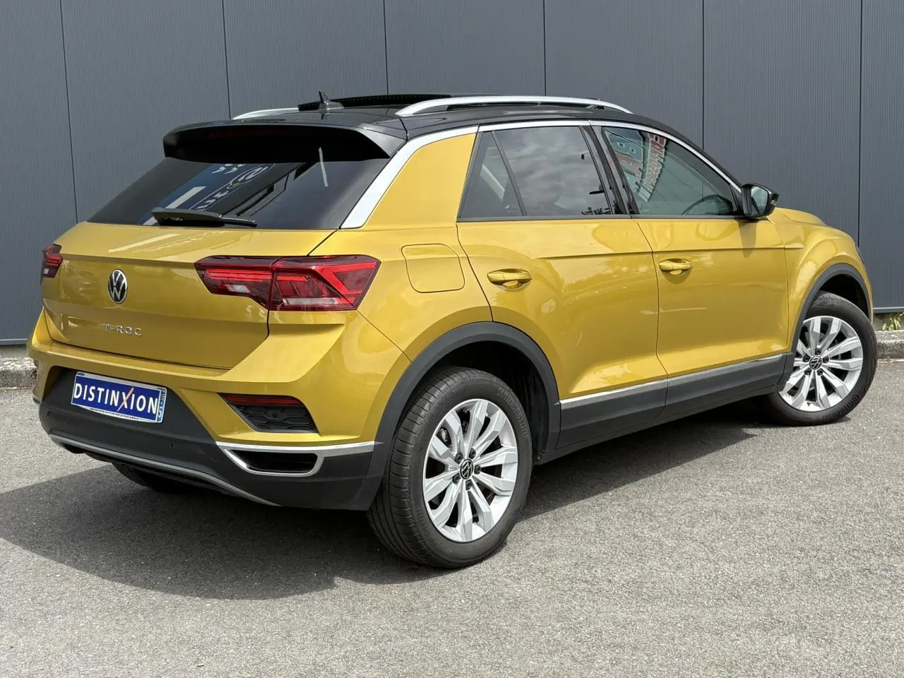 Vue 3/4 arrière droite d'un Volkswagen T-Roc jaune curcuma avec toit noir et jantes alliage 17 pouces.
