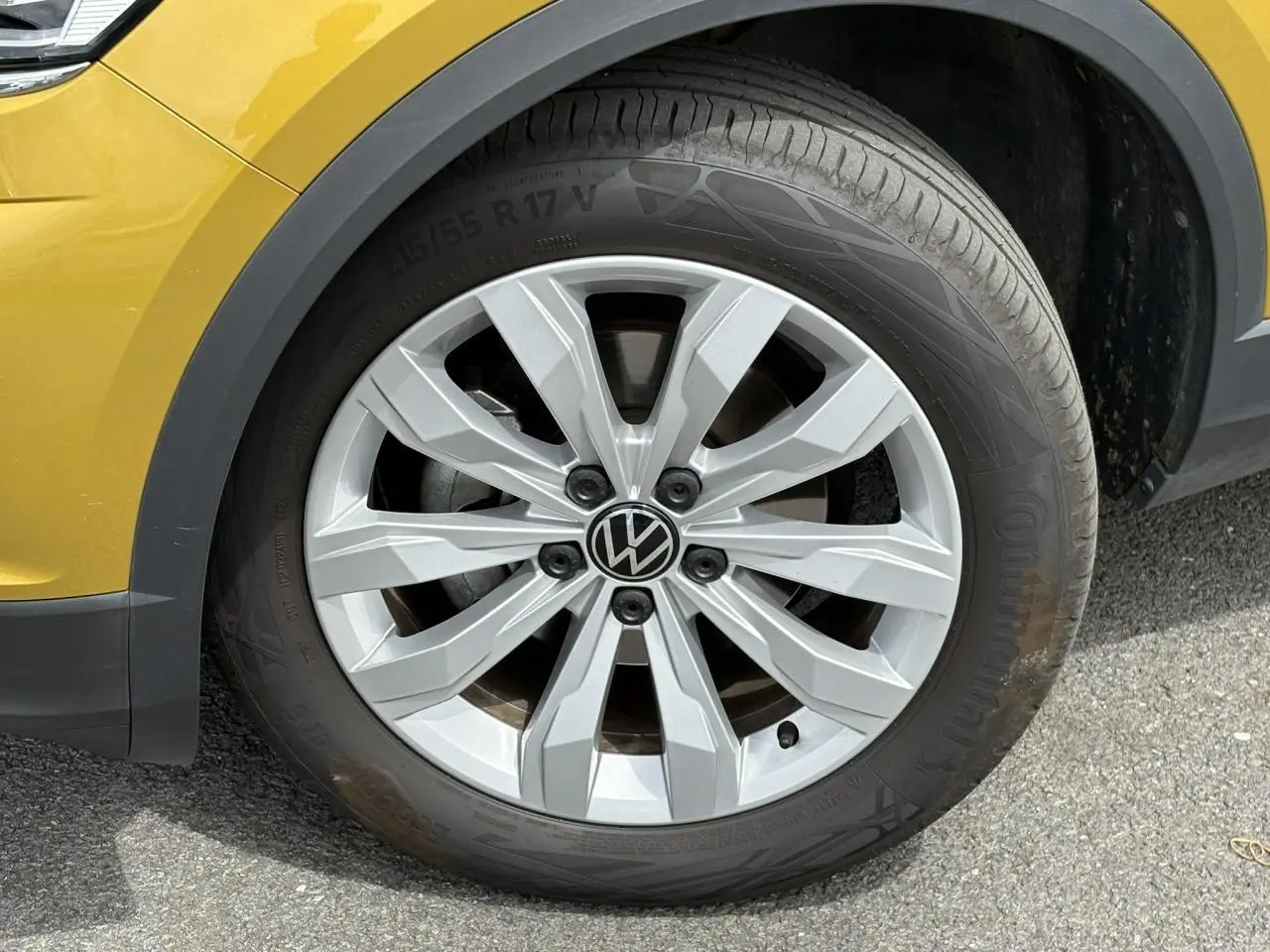 Gros plan sur la roue avant gauche d’un Volkswagen T-Roc jaune curcuma avec jante alliage 17 pouces et logo VW central.