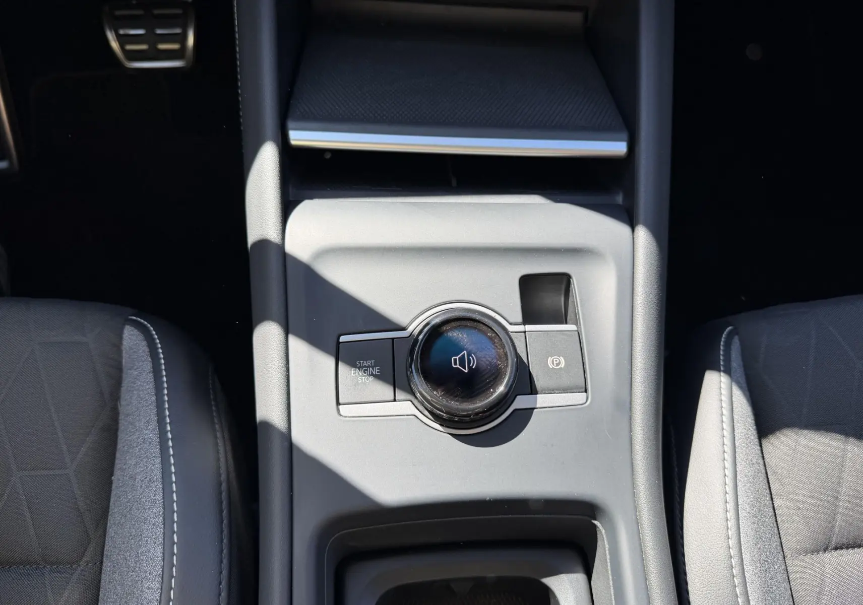 Vue plongeante sur la console centrale grise du Volkswagen Tiguan 2025 avec bouton start/stop et molette de contrôle audio.