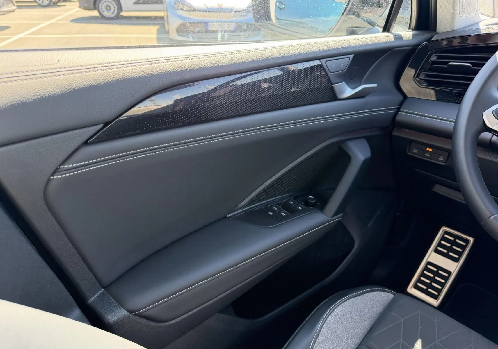 Vue intérieure côté conducteur du Volkswagen Tiguan 2025, montrant la porte en cuir noir avec surpiqûres blanches et commandes électriques.