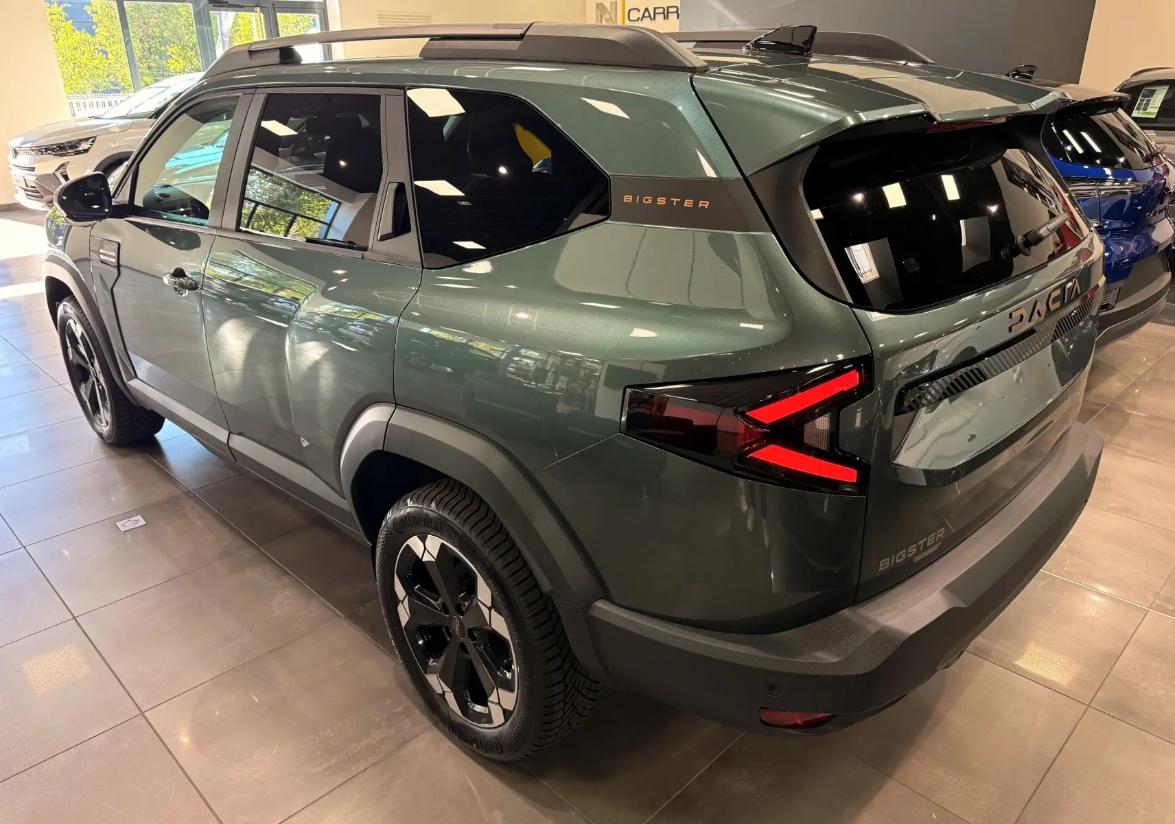 Vue 3/4 arrière droite du Dacia Bigster Hybrid-G 150 4x4 en vert cèdre avec feux arrière LED et jantes noires bicolores.