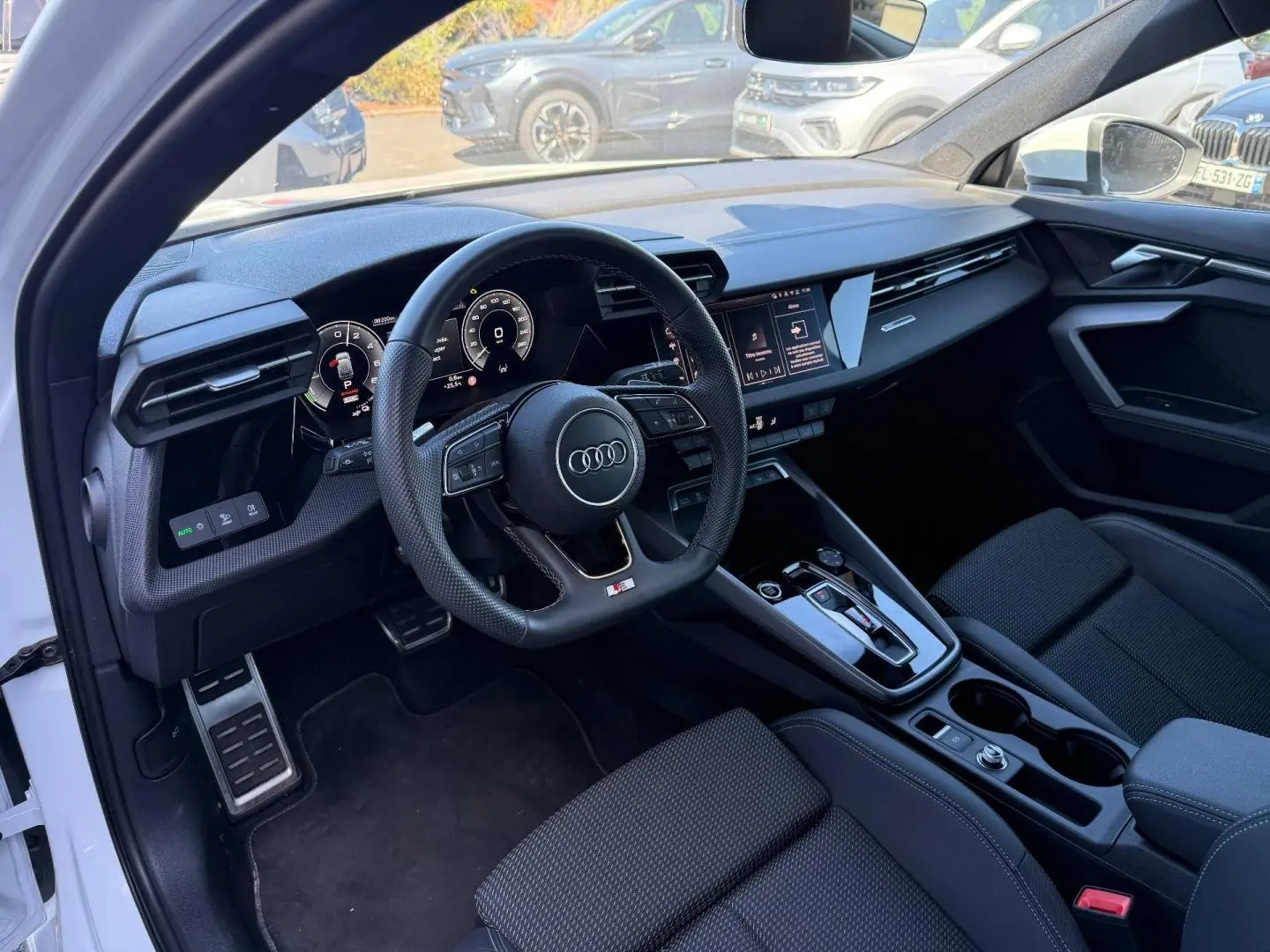 Intérieur Audi A3 Sportback blanc, vue côté conducteur montrant tableau de bord noir et volant sport multifonction.