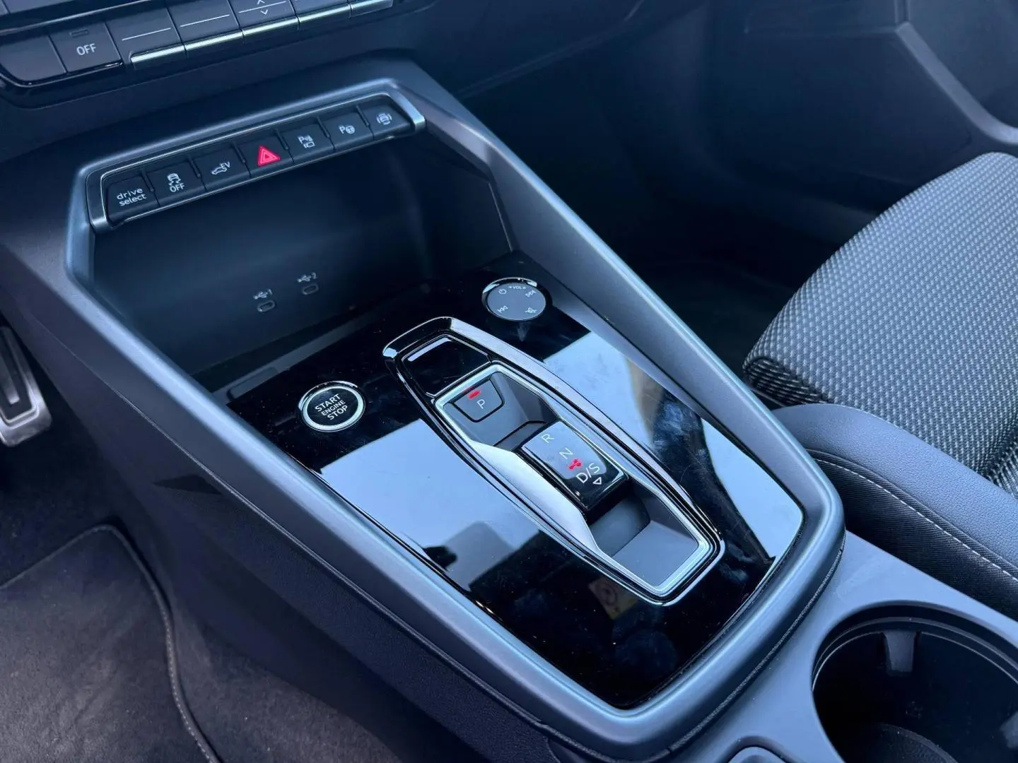 Vue rapprochée de la console centrale noire brillante avec levier de vitesses automatique et bouton start/stop d’une Audi A3 Sportback.