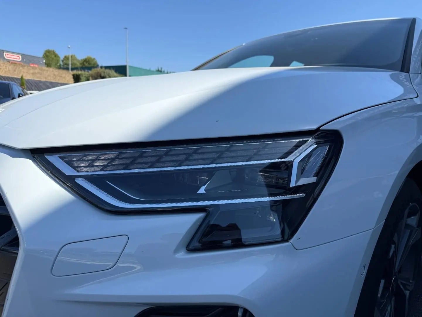 Gros plan sur le phare avant droit d'une Audi A3 Sportback blanc Glacier métallisé, avec jante alu visible en arrière-plan.