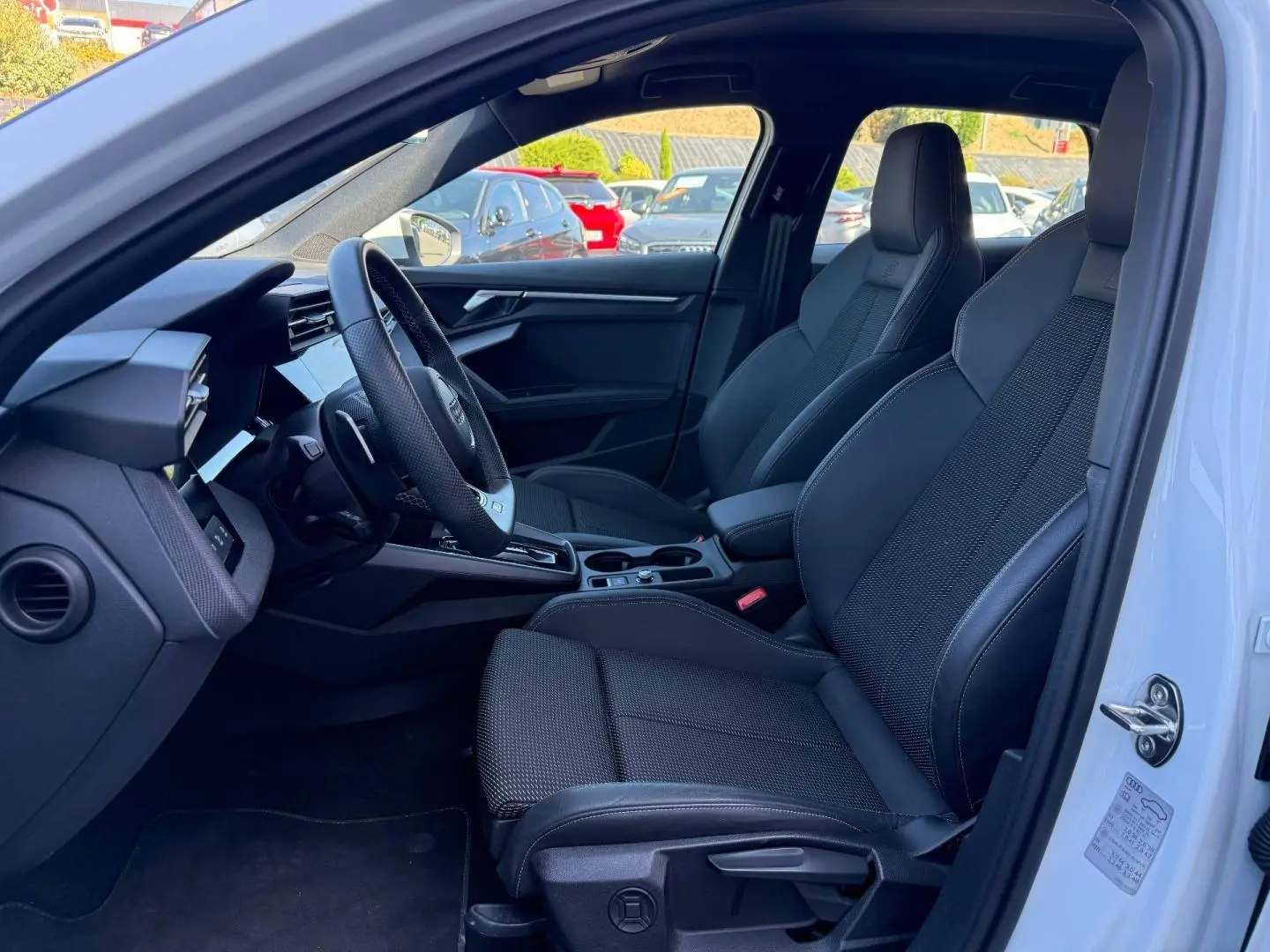 Vue intérieure côté conducteur de l'Audi A3 Sportback 2025, sièges sport noirs et volant cuir multifonction.