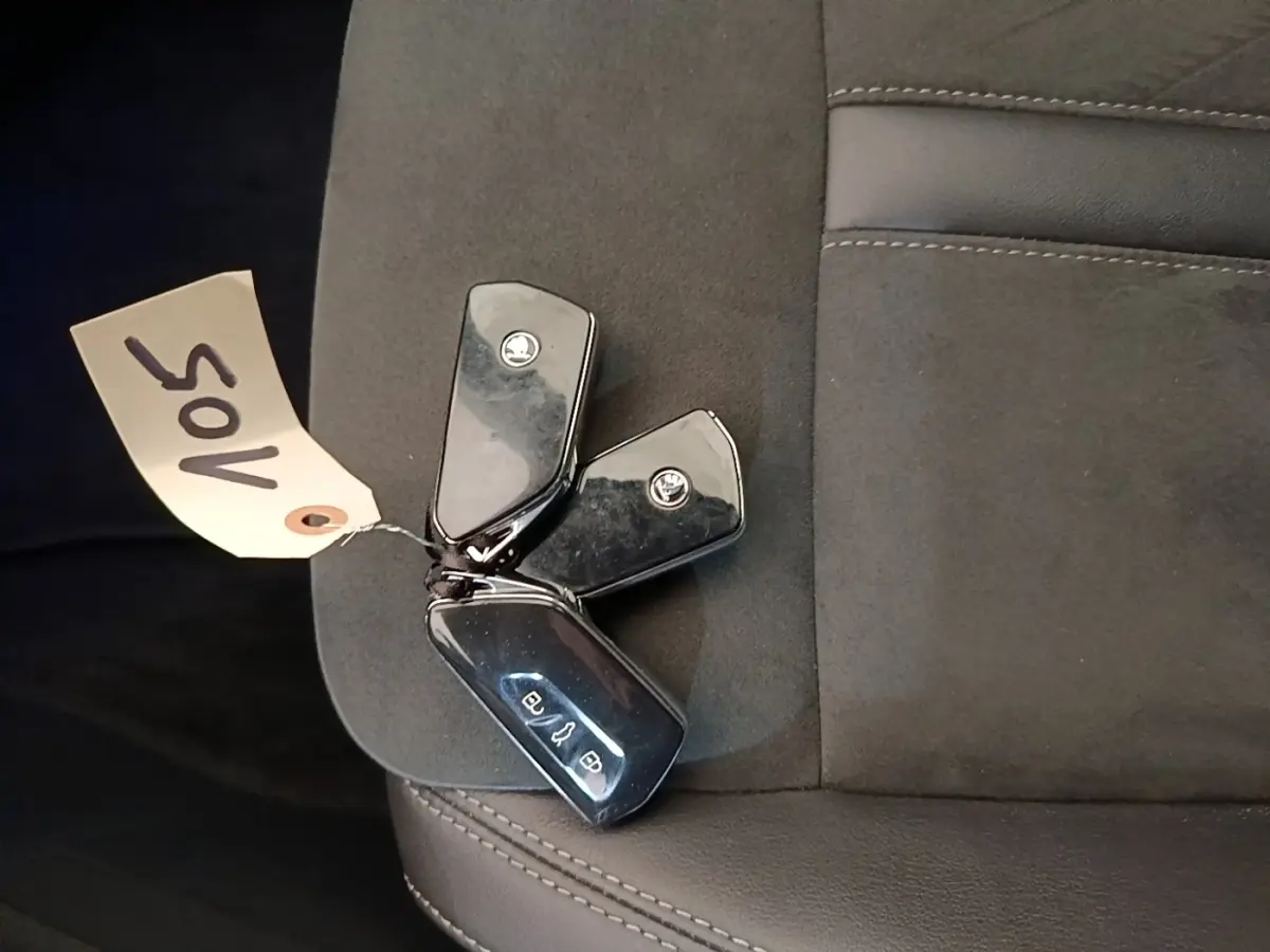Gros plan sur trois clés noires SKODA posées sur un siège en tissu gris foncé, sans vue du véhicule.