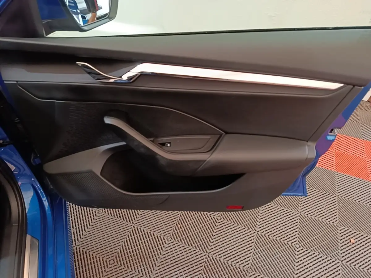 Vue intérieure de la porte avant gauche d’une Skoda Octavia bleu 2022 avec garniture noire et insert chromé.