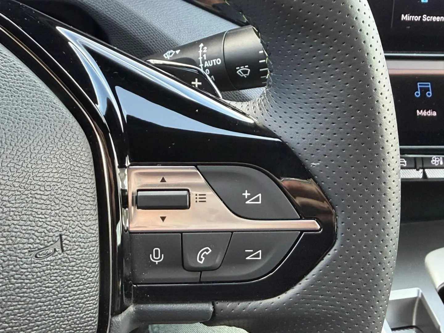 Gros plan sur les commandes multifonctions noires et chrome du volant cuir perforé côté gauche du Peugeot 408 Hybrid 2025.
