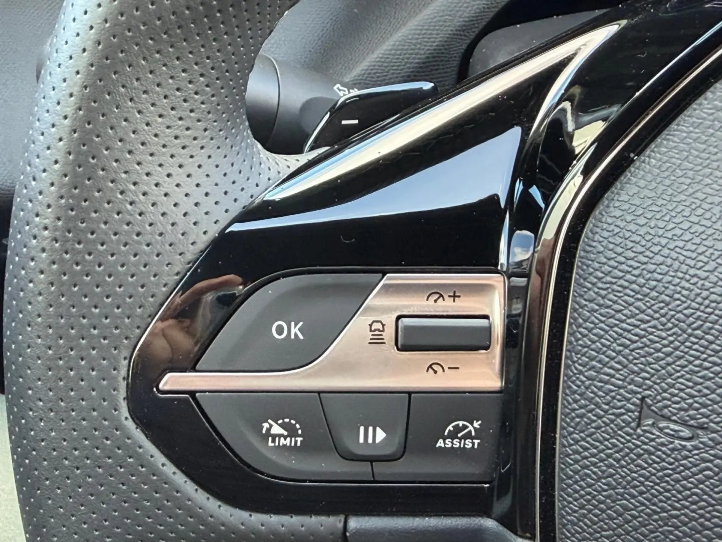 Gros plan sur les commandes de régulateur de vitesse au volant perforé noir de la Peugeot 408 Hybrid 2025.