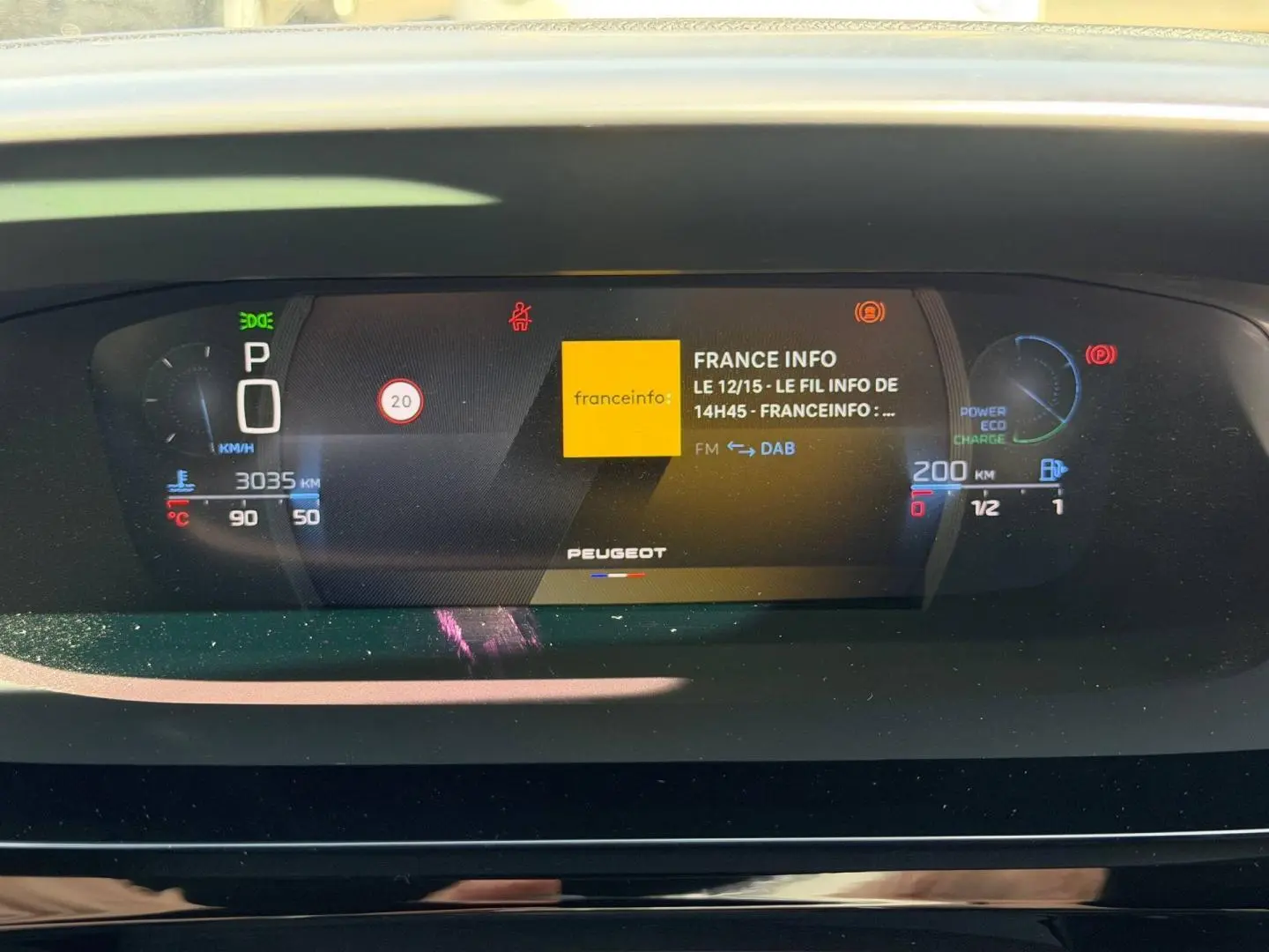 Affichage numérique du tableau de bord Peugeot 408 Hybrid 145ch GT, montrant la radio France Info et les indicateurs de vitesse et batterie.