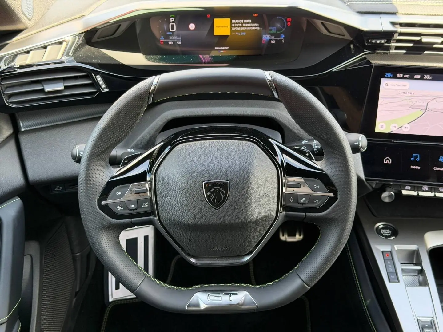 Vue intérieure centrée sur le volant cuir noir GT avec coutures vertes et tableau de bord numérique du Peugeot 408 Hybrid 2025.