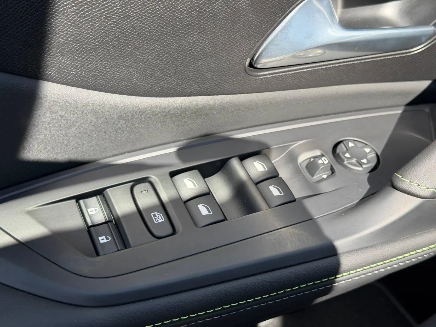 Commande des vitres et rétroviseurs sur la porte côté gauche d’une Peugeot 408 Hybrid 2025 avec surpiqûres vertes.