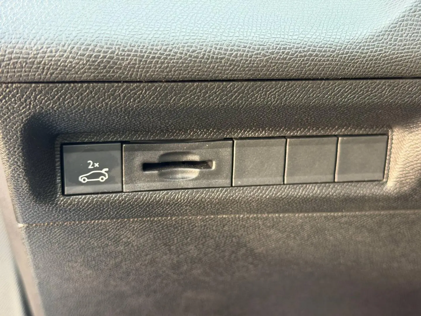 Bouton d'ouverture électrique du coffre sur tableau de bord noir du Peugeot 408 Hybrid 2025.