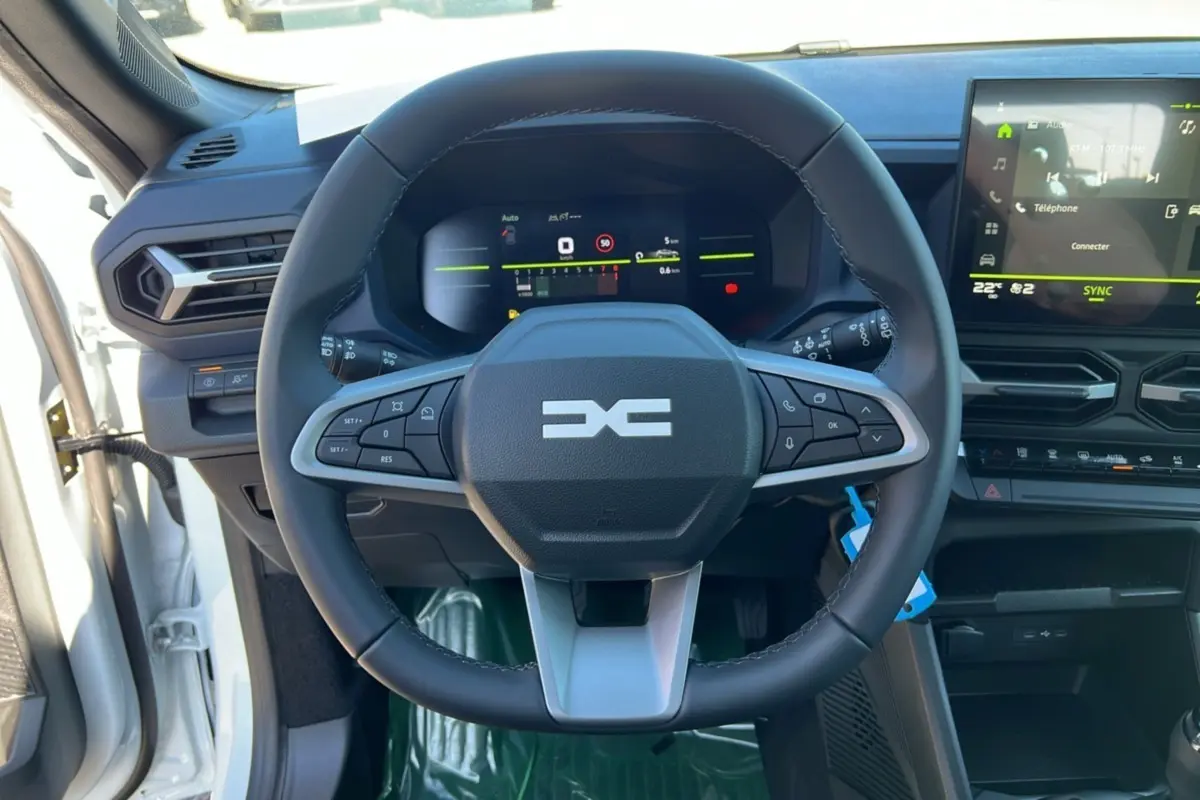 Vue centrée sur le volant du Dacia Bigster blanc glacier 2025, avec tableau de bord numérique et écran tactile visible.