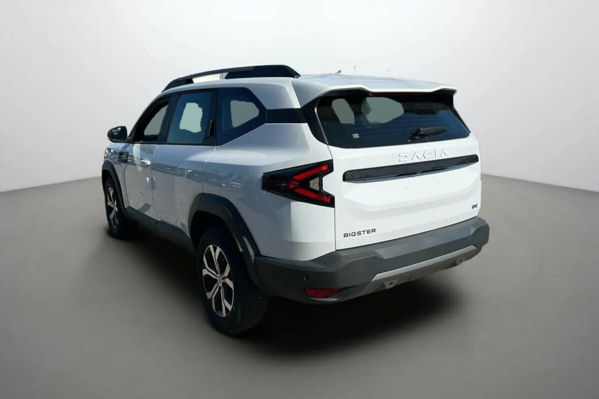 Vue 3/4 arrière droite du SUV Dacia Bigster blanc glacier avec feux arrière en forme de flèche et barres de toit noires.