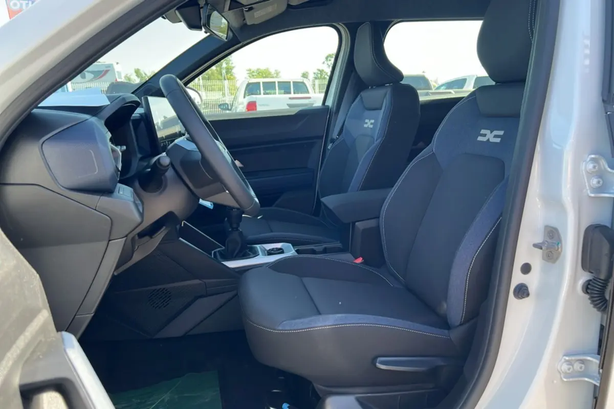 Intérieur du Dacia Bigster blanc glacier vu côté conducteur, sièges noirs avec logo DC et boîte manuelle visible.