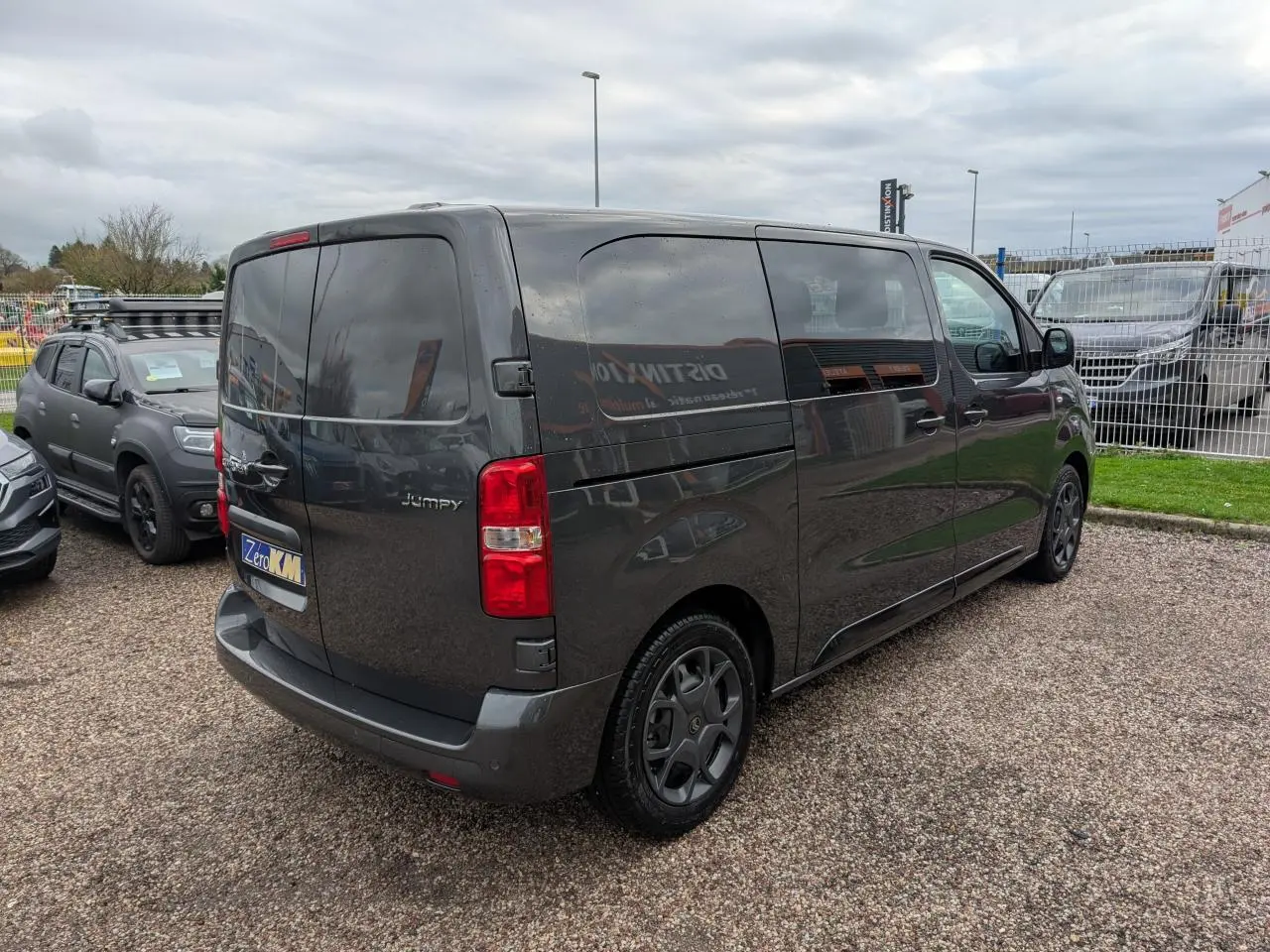 Vue 3/4 arrière droite d'un Citroën Jumpy gris foncé avec portes arrière battantes et vitres teintées.