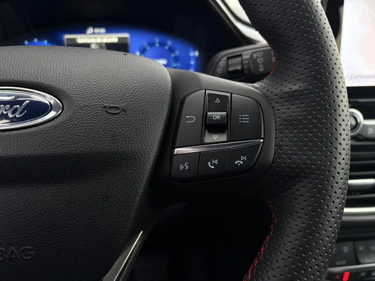 Gros plan sur le volant perforé noir avec surpiqûres rouges du Ford Puma 2023, boutons de commande visibles.