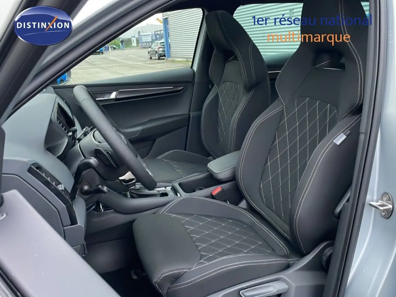 Vue intérieure côté conducteur du Skoda Karoq gris argent 2025, sièges sport noirs avec surpiqûres blanches.