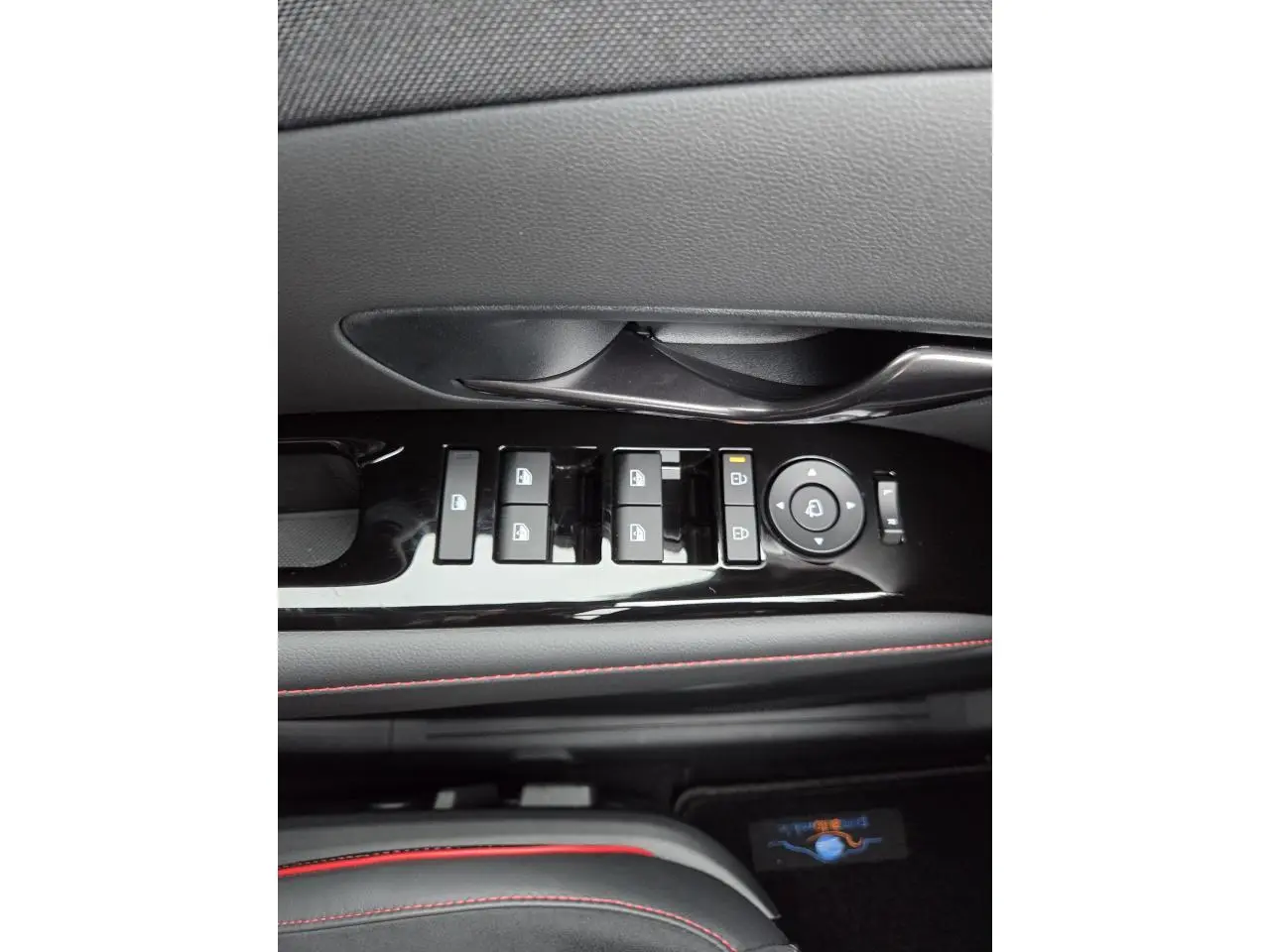 Gros plan sur les commandes de lève-vitres et rétroviseurs côté conducteur du Hyundai Tucson gris avec surpiqûres rouges.