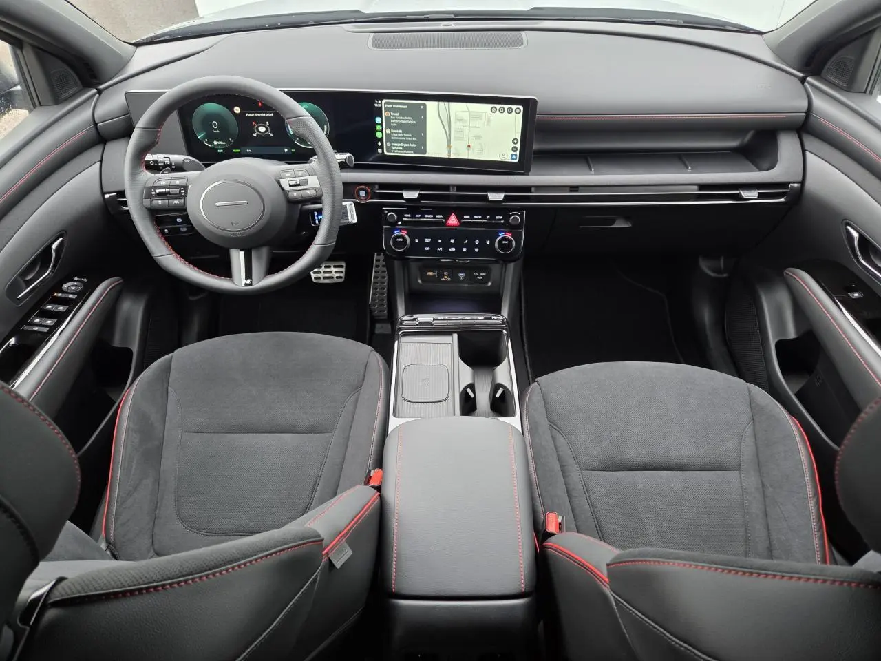 Vue intérieure frontale du Hyundai Tucson N Line 2025, avec sellerie cuir/alcantara noire et surpiqûres rouges, tableau de bord numérique et écran tactile large.