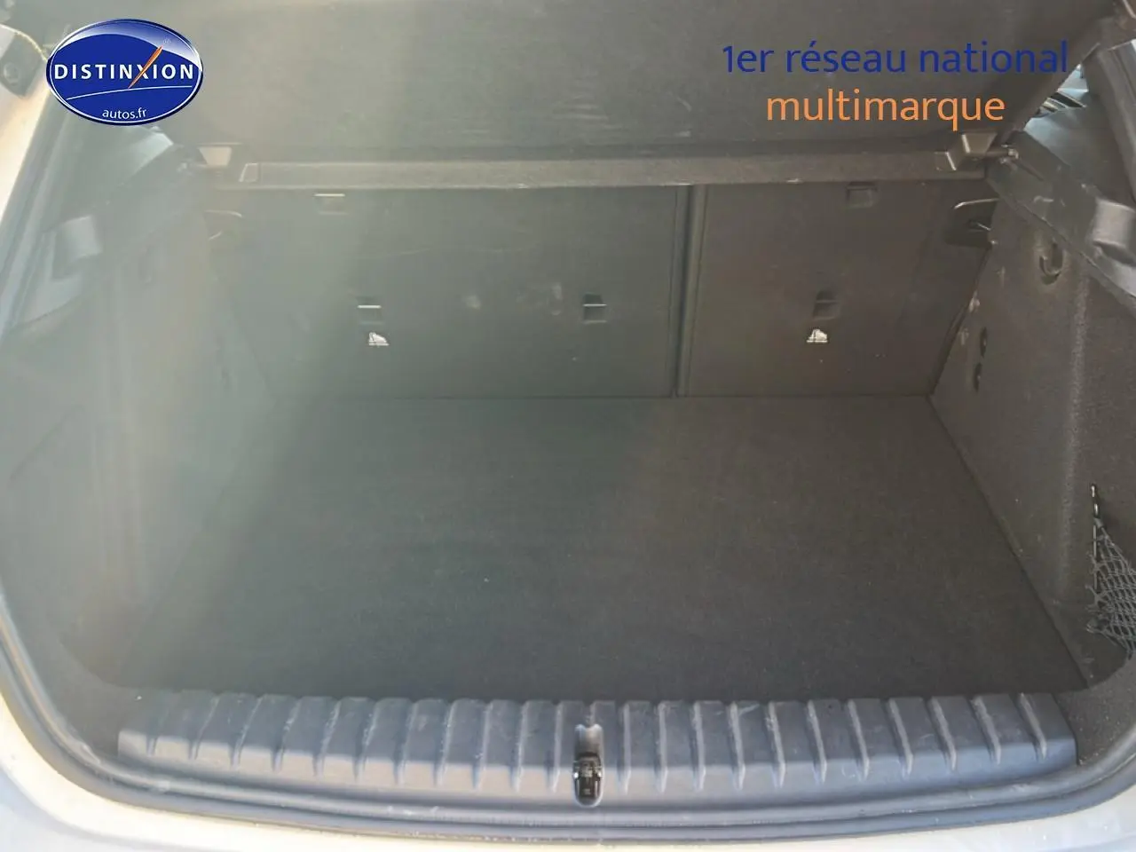 Coffre ouvert vu de l'arrière d'une BMW Série 1 blanche, montrant un espace de chargement propre et vide.