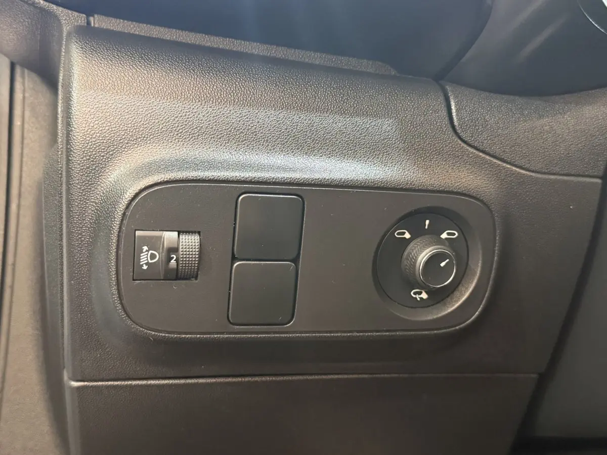 Gros plan sur les commandes noires de réglage des phares et des rétroviseurs dans une Citroën C3 blanche, côté conducteur.
