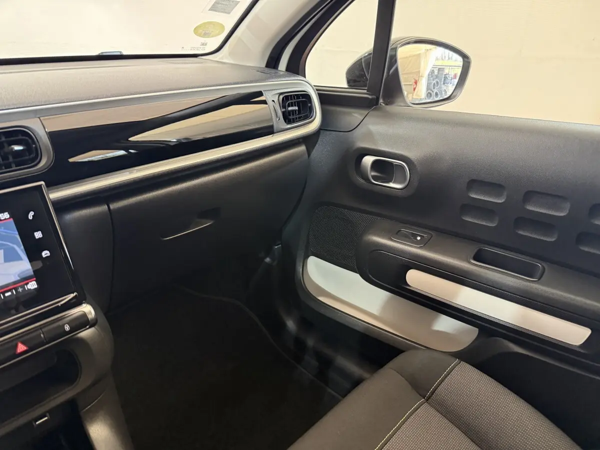 Vue intérieure côté passager de la Citroën C3 blanche 2021, avec tableau de bord noir brillant et détails modernes.