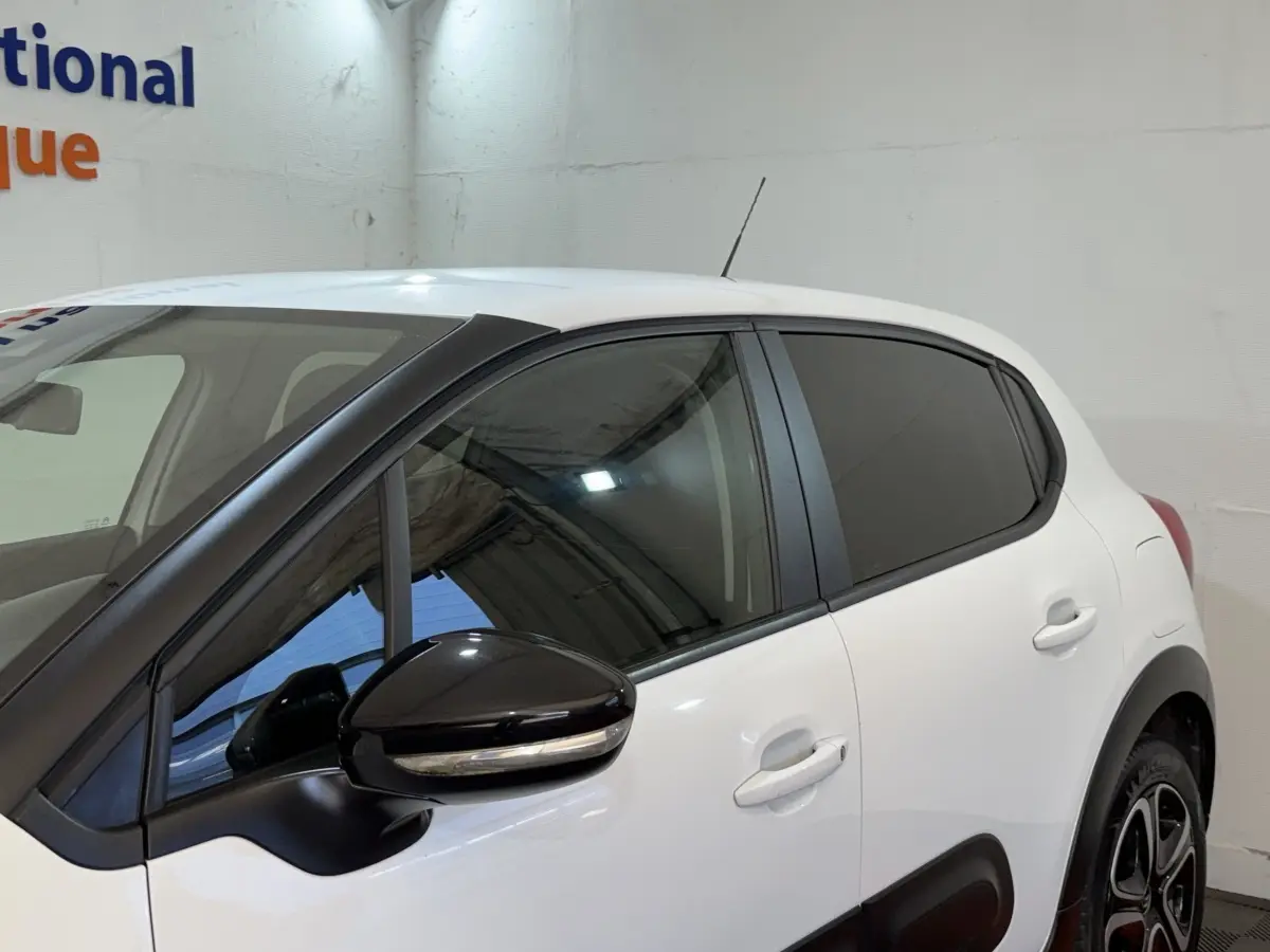 Vue de profil côté gauche d'une Citroën C3 blanche avec rétroviseur noir et vitres teintées dans un garage.